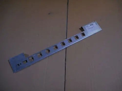 Metallplatte mit mehreren Ausschnitten, die für Montagezwecke verwendet wird. Teil eines Remeha Produkts zur Verrohrung, auf braunem Karton unterlegt.